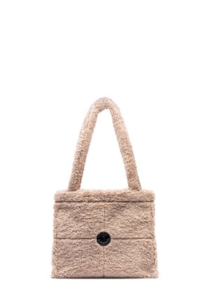 Beige rechthoekige tote bag met een pluizige textuur, een enkele brede handgreep en een gecentreerde ronde zwarte logo patch aan de voorkant.