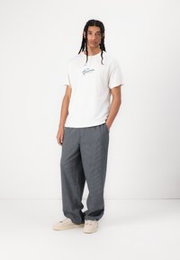White cotton T-shirt with "Groceries" logo in blue, paired with loose-fit, navy and white striped trousers, and beige sneakers.
