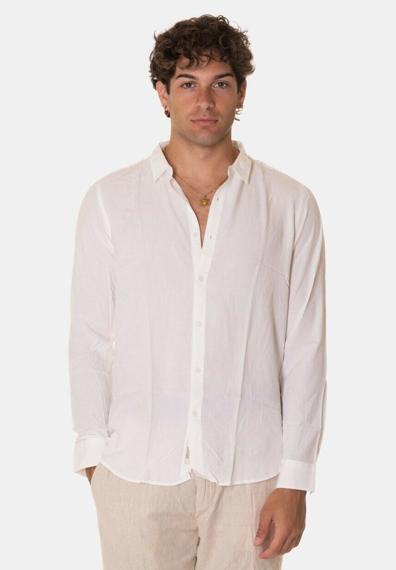 Camicia bianca a maniche lunghe con bottoni, realizzata in tessuto leggero, dotata di colletto classico, patta frontale e polsini con un solo bottone.