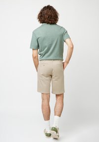 Camisa polo verde de manga corta y pantalones cortos beige. La camisa tiene una tela texturizada; los pantalones cortos tienen bolsillos traseros y un ajuste recto.