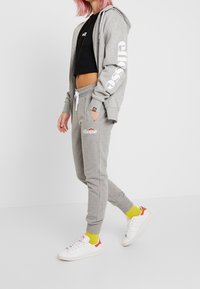 Gray matching hoodie and jogger set in soft fabric, featuring logo prints. White sneakers and yellow ankle socks. Modern, fitted design.