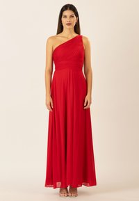 Rotes, einseitig beschnittenes Abendkleid aus fließendem Stoff, mit geraffter Textur am Oberteil und einem langen, A-Linien-Rock. Silberne, offene High Heels.