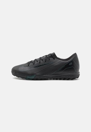 Chaussure de football noire à coupe basse avec dessus texturé, fermeture à lacets et semelle extérieure en caoutchouc conçue pour jouer sur terrain ferme.
