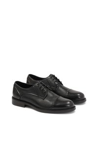 Scarpe in pelle nera con finitura liscia, punte arrotondate e superficie texturizzata. Caratterizzate da chiusura con lacci e suola in gomma a profilo basso.