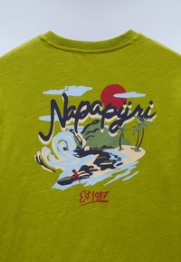 Πράσινο κοντομάνικο μπλουζάκι με ζωντανό γραφικό τύπωμα μιας παραλιακής σκηνής, με κύματα, έναν κόκκινο ήλιο και το κείμενο "Napapijri" με έντονους χαρακτήρες.