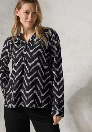Haut à manches longues noir et blanc avec un motif en zigzag, col classique et fermeture à boutons. Texture douce, coupe droite.