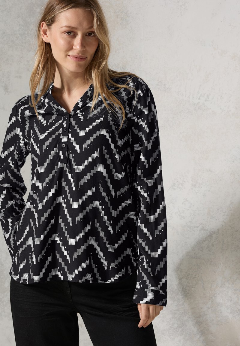 Maglietta a maniche lunghe bianco e nero con motivo a zigzag, colletto e chiusura con bottoni. Tessuto morbido, taglio dritto.