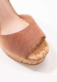Růžové semišové sandály na klínu s širokým otevřeným špičkou a korkovou platformou. Texturovaný svršek s hladkými, zakřivenými okraji a jemnými detaily v prošívání.