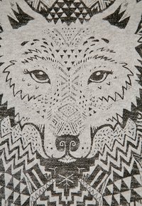 T-shirt graphique avec un motif de loup en encre noire sur un tissu gris clair. L'œuvre comprend des motifs géométriques et des lignes nettes autour du visage du loup.