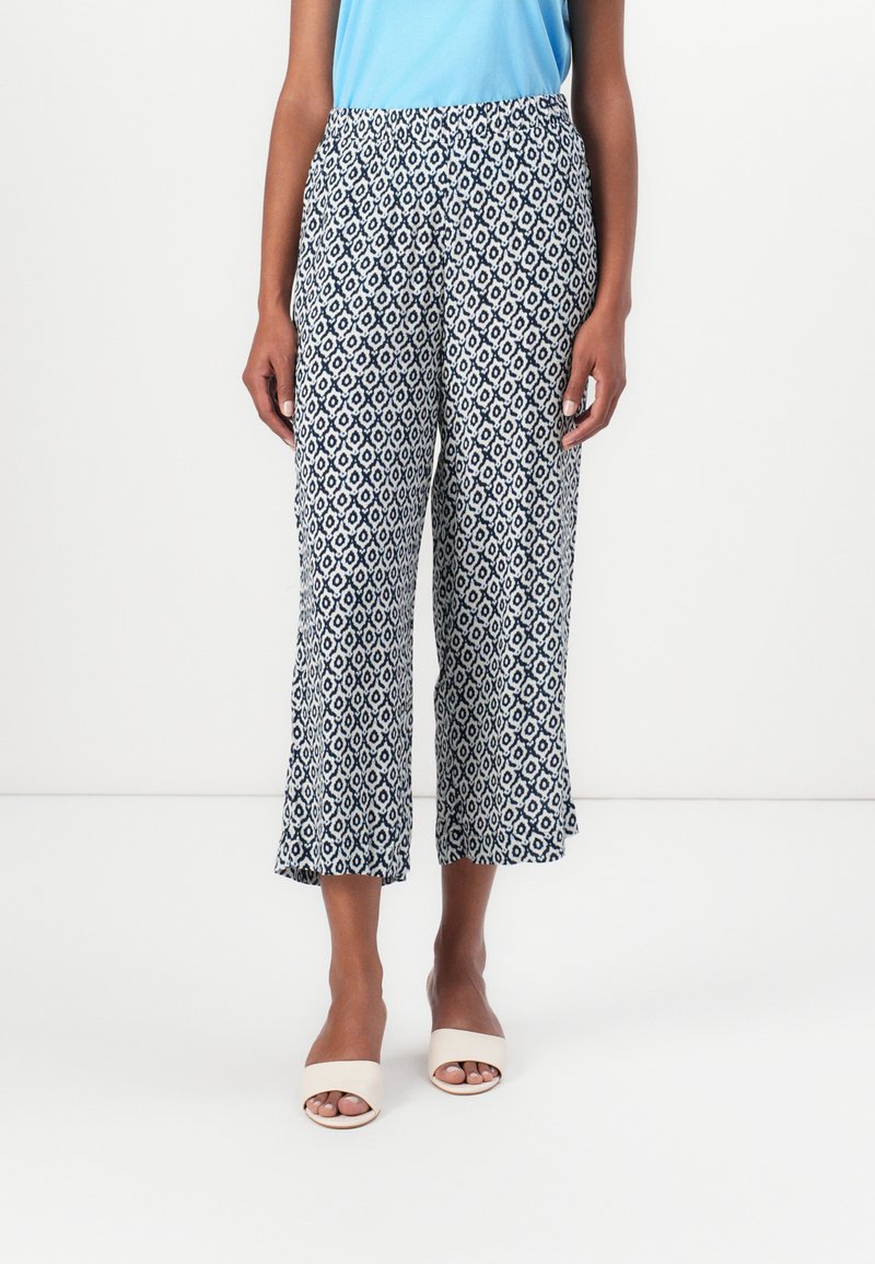Pantaloni cropped a fantasia in bianco e navy, caratterizzati da un design geometrico, cintura elastica e orlo svasato, abbinati a sandali con punta aperta.