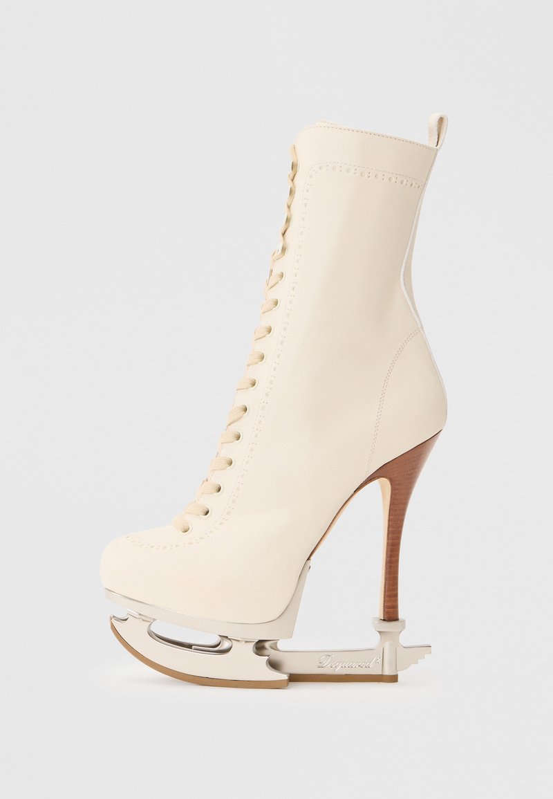 Botte de patin à glace en cuir crème avec un talon haut et une lame en argent. Présente un laçage à l'avant et une couture décorative le long de la tige.