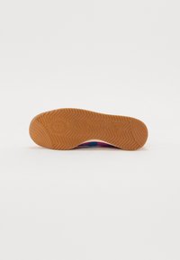 Semelle de chaussure de sport multicolore avec une surface en caoutchouc gomme texturée. Présente un motif en chevrons et un logo de marque en relief au centre.
