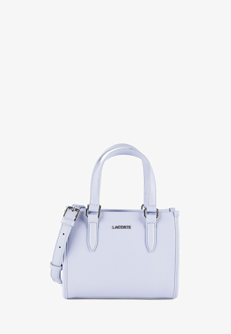Petit sac à main en cuir violet clair avec ferrures argentées, double poignée supérieure, bandoulière réglable et logo "LACOSTE" sur le devant.