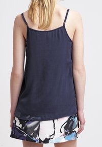 Granatowy top bez rękawów wykonany z lekkiego materiału, posiada regulowane ramiączka oraz zaokrąglony dół, w połączeniu z wzorzystą spódnicą.