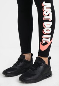 Beine in schwarzen Sneakern und schwarzen Leggings mit großem pinkem "JUST DO IT."-Text am rechten Bein vor einem weißen Hintergrund.