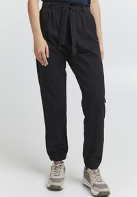 Black, lightweight, elastic-waist jogger pants with a tied belt, elastic cuffs, and side pockets, paired with gray and white sneakers.