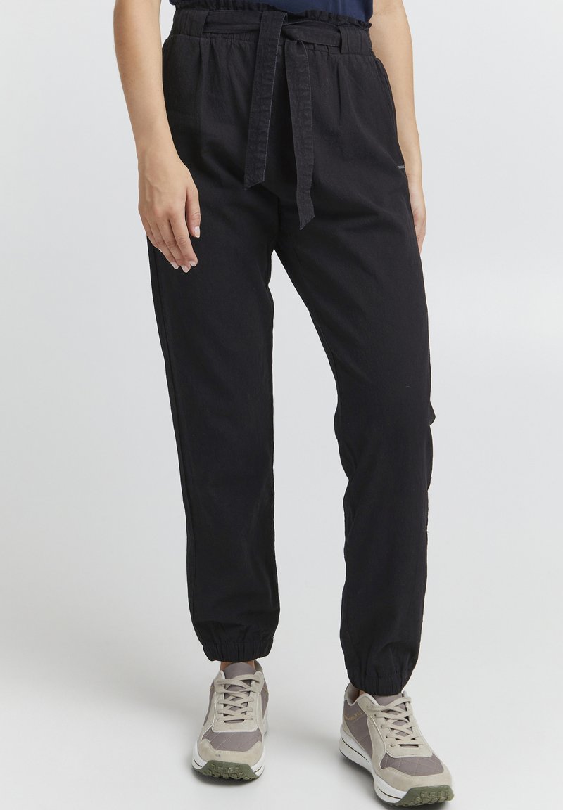 Black, lightweight, elastic-waist jogger pants with a tied belt, elastic cuffs, and side pockets, paired with gray and white sneakers.
