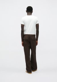 Biała koszulka z krótkim rękawem zestawiona z brązowymi spodniami o szerokich nogawkach z tylnymi kieszeniami. Spodnie mają gładką fakturę i luźny krój.