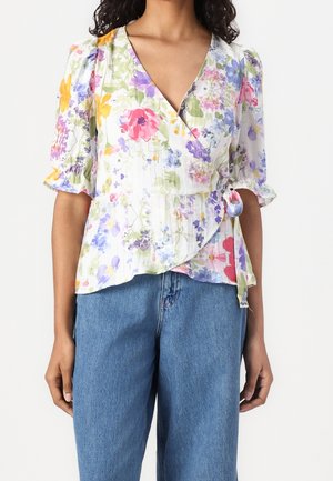 Femme portant un chemisier à fleurs à manches mi-longues bouffantes, associé à un jean taille haute bleu.