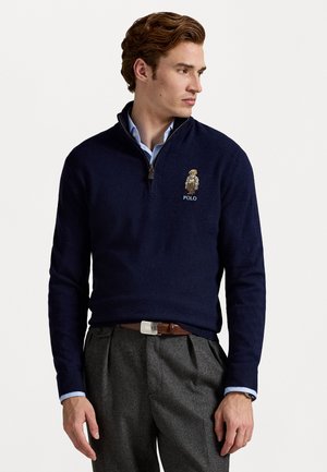 Navy zip-up trui met een hoge kraag, voorzien van een klein geborduurd Polo-logo en een gedetailleerde afbeelding van een personage op de borst.