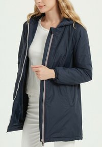 Doudoune bleu marine avec capuche, dotée d'une fermeture éclair intégrale et de poches latérales. Tissu lisse et léger avec des poignets élastiques.