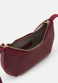 Borsa a mano in pelle rossa con finitura textured, zip dorata e tasca interna. Forma curva con una tracolla sottile.