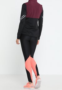 Długi rękaw sportowy top w kolorze czarnym z bordowym panelem i refleksyjnymi akcentami, połączony z dopasowanymi legginsami w kolorze czarnym i różowym w designie color-block.