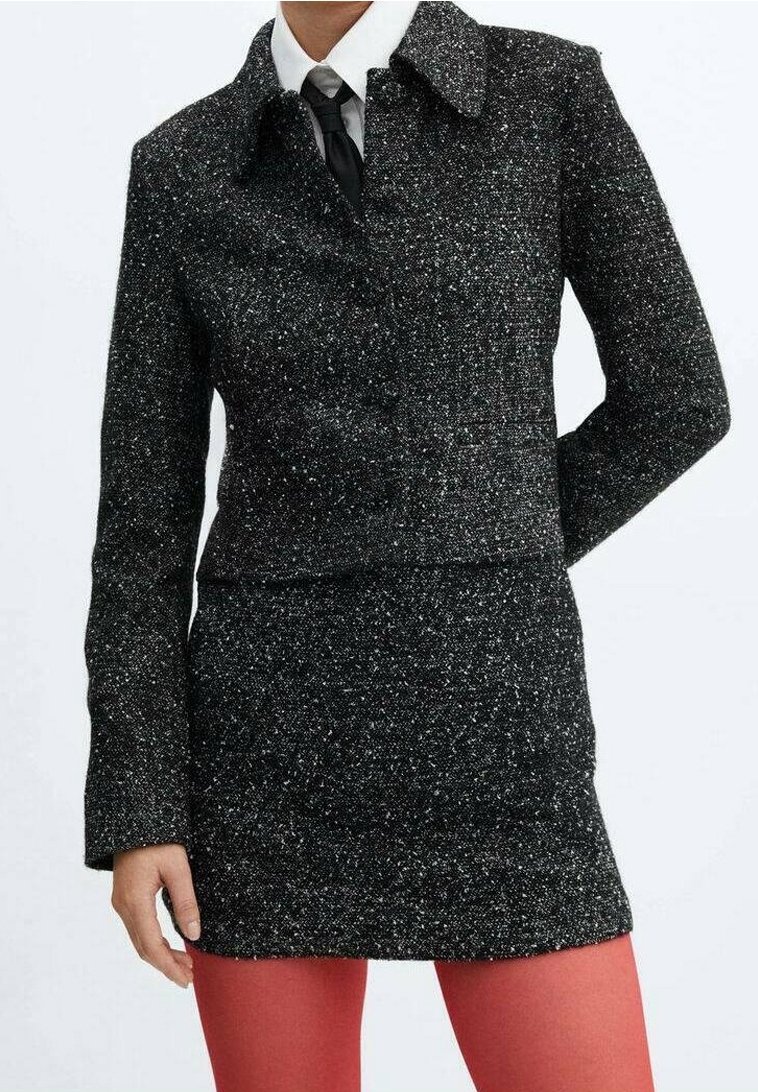 Veste en tweed noir et blanc à motifs tachetés, avec col chemise, fermeture à un bouton et manches longues, associée à une jupe ajustée assortie.