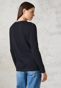 Svart stickad tröja med ett texturerat mönster, långa ärmar och rundad halsringning. Kombinerad med ljusblå jeans som har en avslappnad passform.