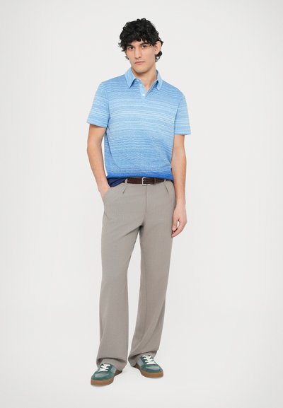 Svetlomodrá pruhovaná polokošeľa, sivé plisované nohavice a zelené semišové tenisky s bielymi šnúrkami. Hnedý opasok dopĺňa outfit.