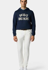 Námořnická mikina s textem "BROOKS BROTHERS", bílé bavlněné kalhoty a bílé tenisky. Mikina má šňůrku, volný střih a žebrované manžety.