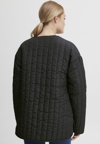 Svart kviltet jakke med avslappet passform. Har rund halslinning og lange ermer, med synlige sømmer over stoffet.