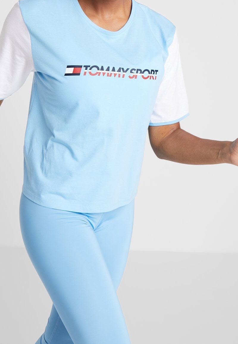 Světle modré tričko s krátkými bílými rukávy, na kterém je červené a námořnické logo "TOMMY SPORT". Vydáváno s odpovídajícími světle modrými legínami.