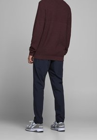 Bordowy sweter o teksturowanej powierzchni, granatowe spodnie oraz szare buty sportowe z białymi sznurowadłami, widziane od tyłu. Prosty design o luźnym kroju.