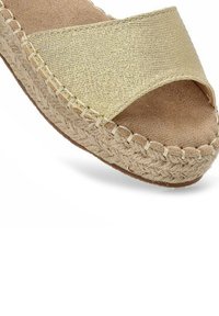 Espadrille de tela dorada tejida con un diseño de tiras cruzadas y una suela de yute beige. El suave interior de ante crea un ajuste cómodo.