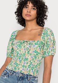 Blusa com padrão floral em verde e azul, com mangas bufantes, decote quadrado e detalhe em laço à frente. Feita de tecido leve.
