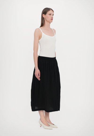 Sort plisseret midi nederdel med elastisk talje, parret med en hvid tanktop og cremefarvede hæle. Glat stof, afslappet design.