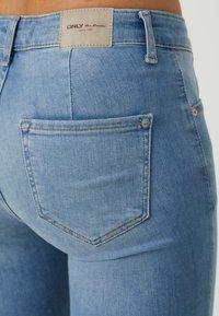 Vaqueros de mezclilla azul claro con una forma ligeramente ajustada, que cuentan con un único bolsillo trasero y una etiqueta de cuero en la cinturilla.