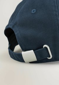 Căciulă bleumarin dintr-un material texturat, cu o cataramă metalică argintie și o curea la spate pentru ajustarea dimensiunii și orificii de ventilație.