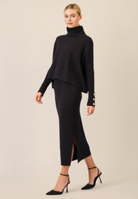 Zwarte gebreide turtlenecktrui met een ruime silhoutte en ribbelstructuur, gecombineerd met een bijpassende kokerrok met zijsplitten.