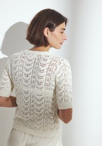 Maglione corto a maniche corte in bianco sporco, con un motivo a maglia aperta texturizzata, scollatura a girocollo e orlo a coste.