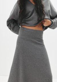 Grå strikket crop top med lange ærmer, parret med en matchende højtaljet nederdel, begge i et blødt, glat stof med en let stræk.