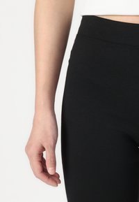 Black leggings made of stretchy, soft fabric, featuring a smooth waistband and fitted design. Hand positioned near the waistband.