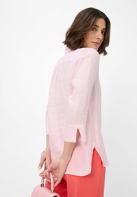 Light pink linen shirt with a collar, three-quarter sleeves, and side slits. The model holds a small pink handbag.