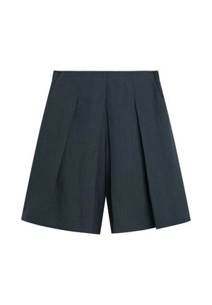 Kvinde iført ærmeløs beige strik top, sort midinederdel, sorte sko og holder en beige clutch, stående mod en ensfarvet lys baggrund.
