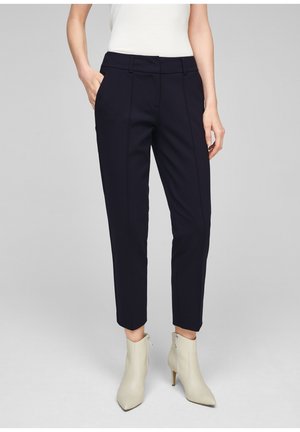 Pantalones azules marino a medida con corte recto, con bolsillos delanteros y pliegues sutiles. Combinados con botines de color claro.