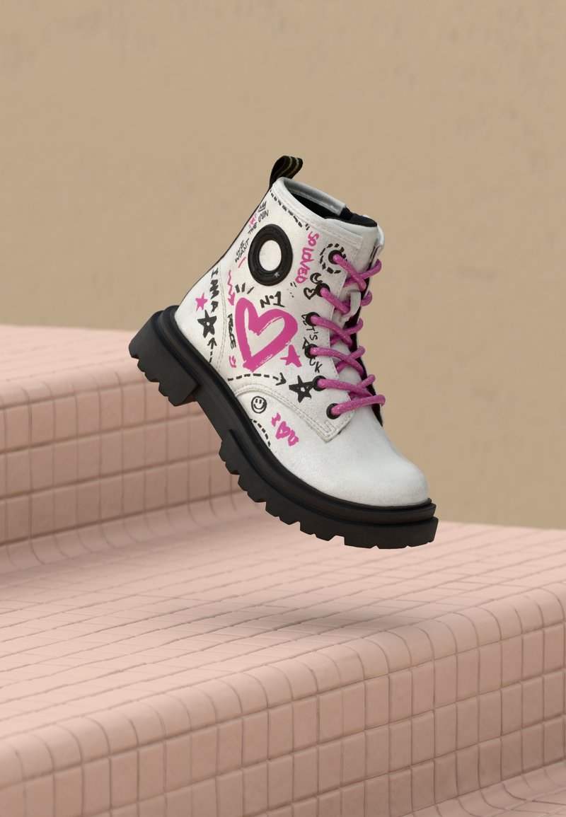 Białe wojskowe buty z różowymi sznurówkami oraz czarnymi sercami w stylu graffiti, gwiazdkami i uśmiechami, unoszące się nad różowymi kafelkami na schodach.