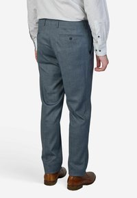 Graue, maßgeschneiderte Hose aus strukturiertem Stoff, mit flacher Vorderseite, zwei Gesäßtaschen und geschmackvollem Schnitt, kombiniert mit braunen Schuhen.