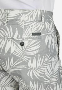 Graue Shorts mit weißem Blattmuster, mit einer Gesäßtasche mit einem schwarzen Knopf und einem kleinen Markenetikett. Hergestellt aus strukturiertem Stoff.