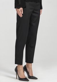 Czarne eleganckie spodnie o wąskim kroju, wykonane z gładkiego materiału, z zagięciem na przodzie, w zestawie z czarnymi czółenkami na obcasie.